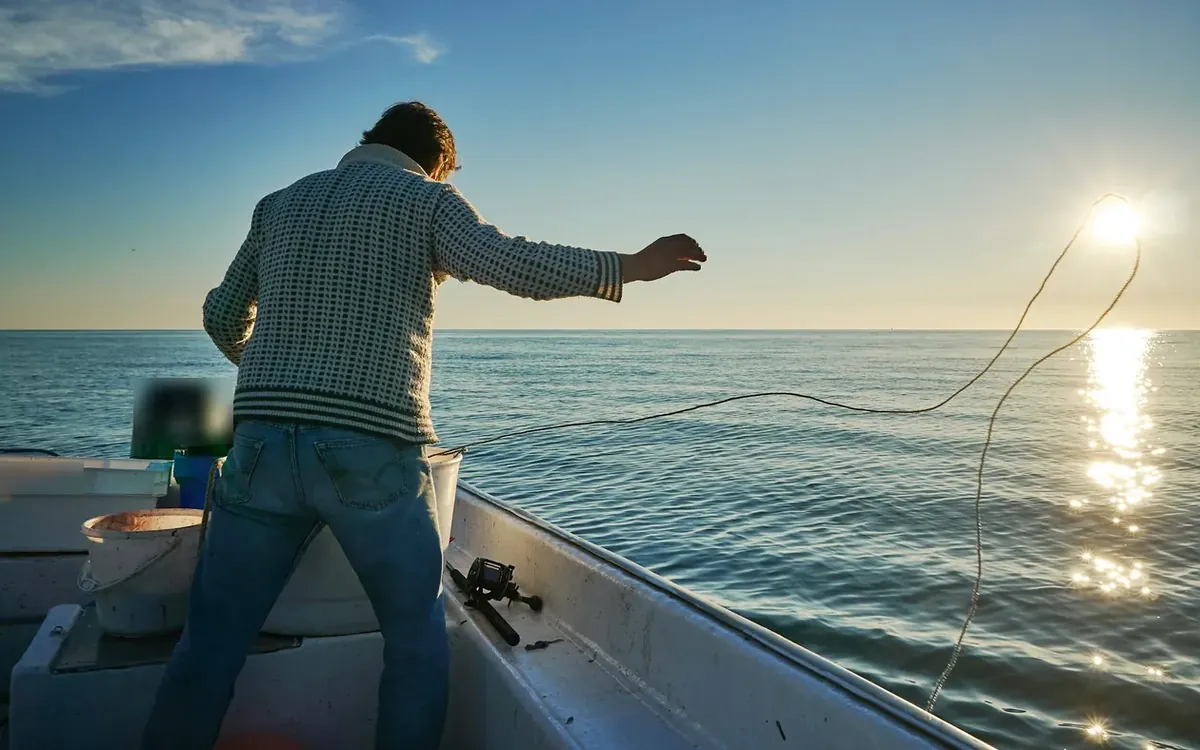 Visser werpt uit vanaf een kleine open boot op kalme zee bij laagstaande zon